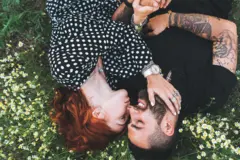 Two young lovers lying on a field share an intimate kiss surrounded by a blanket of daisies capturing the essence of romance
