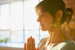 In a serene moment of meditation, a woman channels her inner peace as the warm sunlight filters through the window, casting a gentle glow that enhances the tranquility of her practice