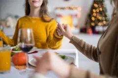In a cozy holiday setting, two friends share a moment of connection over a beautifully set table, surrounded by the warm glow of lights and festive decor