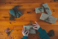 Amidst the warm glow of a wooden table, hands deftly wrap gifts in rustic paper, adorned with natural twine and seasonal greenery, capturing the essence of cozy gatherings and thoughtful surprises