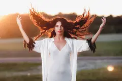 Beautiful woman with long red hair in the field at sunset