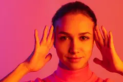 Young woman posing in neon lit studio with hands framing her face