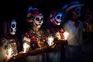 Three women in Catrina costumes, man in cowboy dress, all with skull make-up and candles for day of the dead