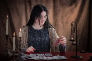 Tarot reader in a dimly lit room placing tarot cards on a table adorned with flickering candles