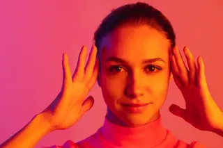 Young woman posing in neon lit studio with hands framing her face