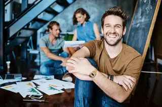 Portrait of a young designer sitting in an office with his colleagues in the background